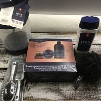 Photo showing all items of the men's grooming lot including Gillette beard grooming kit box, Izod hairbrush, comb, body wash, bath sponge, and carrying bag on a rustic wooden surface.