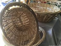Close-up photo showing detail of the oval shape and weaving pattern of three wicker baskets stacked together, highlighting the natural light brown color and woven handles.