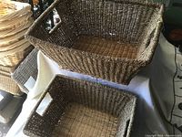 Two new rectangular woven baskets stacked one inside the other on a white cloth and surrounded by other baskets.