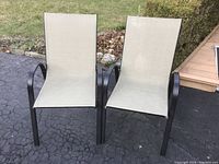 Two outdoor patio chairs with black metal frames and beige fabric seating on driveway surface.