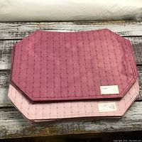 Stack of dark pink and light pink woven placemats showing textured grid pattern and stitched edges with original price tags.