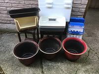 View of plastic items on stone floor, including three planters, cream planter on stand, cooler box, and two storage boxes.