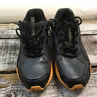 Front view of Puma runners showing black synthetic leather and mesh upper, black laces, and orange outsole.