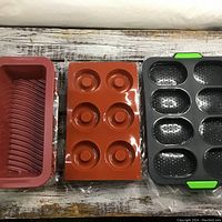 Silicone loaf pans on left, silicone donut pans in middle, metal mini loaf pan with green handles on right.