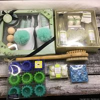 Photo showing two boxed spa gift sets with spa body care products, bath poufs, natural sponges, and bath oils, accompanied by wooden bath brushes and multiple packs of floating candles in green, blue and white.
