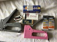 Two light duty staplers - Swingline (silver) and Tangible Co. LT-207 (pink) - with multiple staple boxes in varying brands and sizes.