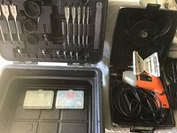 Black & Decker drill stored inside black plastic case with various drill bits, screwdriver bits and small parts container