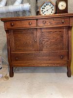 Front view of antique oak chest showing three drawers on top, central double-door cabinet, and bottom drawer. Scrolled legs visible.