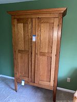 Full view of the light tones wood Shaker style armoire showing double paneled doors and caster wheels at base.