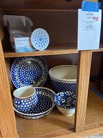 Blue and white pottery pieces including plate, bowls, and coasters displayed inside wooden cabinet shelf.