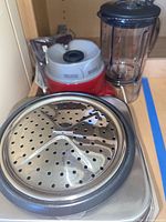 Red Breville blender base with attached control panel and clear pitcher alongside Cuisinart rice cooker steaming tray.