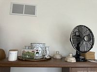 Wide shot showing the black Century brand vintage table fan, Moravian pottery planter and decor, two cream marble candlesticks, and small basket