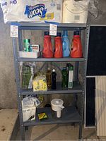 Full shelf shot showing all items included in the lot: paper products on top shelf, cleaning detergents and sponges below, napkins and Brita filter on bottom shelf.