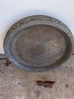 Top view of circular concrete bird bath basin with floral rim detail and metal bird figurine on concrete floor.
