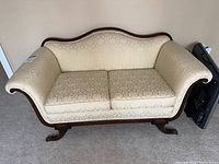 Front view of cream upholstered loveseat with wood frame and carved legs.
