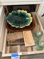 Drawer with two ceramic cabbage leaf bowls, brown square baking dish, green candle holders, wooden molds and tool, fish serving dish visible.