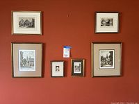 Six gold framed pencil drawings hung on an orange wall, showing various architectural and landscape subjects, some signed.