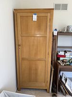 Full view of the light wood closet cabinet showing the exterior door with wooden knob and keyhole.