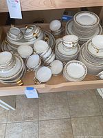 Full set of Theodore Haviland Limoges china stacked on a kitchen cabinet shelf, showing multiple dinner plates, salad plates, bowls, saucers, cups, covered tureen and other serving pieces with gold trim and floral patterns.