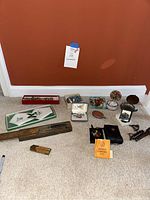 Assorted costume jewelry, jewelry holders, compass with case, and wooden measuring tools arranged on carpet.