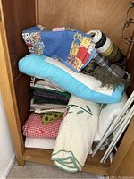 Seven large quilts and fabric pieces stacked inside a wooden cabinet, showing different colors and rolled blankets.