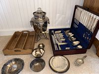 Overview of the lot showing wooden silverware holder with silverware, silver serving pieces, trays, bowls, and tea strainer.