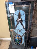 Front view of both stained glass panels leaning against the wall near fireplace, showing designs and size difference.