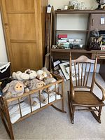 Wooden rocking cradle filled with assorted Steiff stuffed animals next to a child's wooden rocking chair with cane seat, showing front and side views of the cradle with animals visible inside.