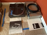 Technics SL-D4 turntable with dust cover placed on carpet with operating instructions and cassette deck with cables nearby.