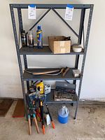 Full view of metal shelving unit showing various items including automotive sprays, tools, batteries, and extension cords.
