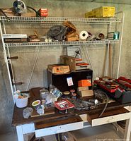 Wide view of metal shelving with boxes, paint, and a wooden tool bench with various tools and items on top.