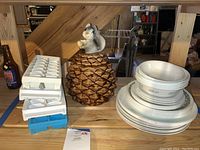 Photo showing stacked Corelle plates and bowls, plastic ice cube trays, and ceramic squirrel cookie jar on pinecone base under basement stairs.