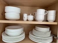 Wood cabinet shelf showing stacks of plates, bowls, cups and servers