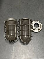 Two vintage industrial light fixtures side by side showing metal cages and glass shades, one fixture detached mounting base plate.