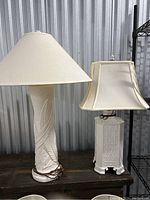 Wide shot of two white table lamps showing overall shape, different bases and lampshades with visible glue yellowing on shades.