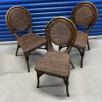 Three brown wicker chairs shown together with round woven backrests and matching woven seats, sitting on concrete floor.