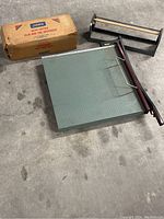 Wide view showing large square table cutter with green cutting grid and two metal dispensers, one dark colored and one with box