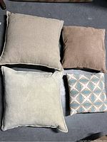 Top-down view of four throw pillows on floor, showing sizes and colors.