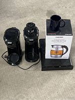 Chefman electric kettle boxed with blue ceramic mug on top, next to two Toastmaster coffee makers and black coffee pod holder.