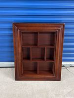 Front view of the wooden framed wall shelf with multiple compartments, dark polished finish.