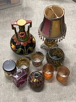 Wide view of lot showing all items on carpeted floor, including the mini stained glass lamp with fabric shade, floral ceramic vase, multiple glass mosaic votive holders, amber votive glasses, glass mosaic bottle and round vase, and scented candle.