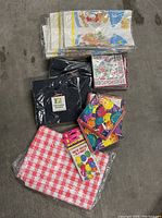 Photo displaying a variety of party supplies including napkins with colorful birthday scenes, red and white checkered tablecloth, black plastic cover, and packs of invitations.