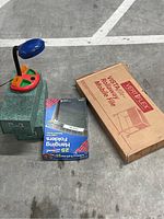 Photo of vertical rolling file cabinet, box of hanging folders, and desk lamp arranged on concrete floor.