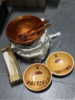 Four stacked wooden salad bowls with wooden spoon and fork serving sets, one snack bowl and one pretzel bowl with colorful painted chef and text designs.