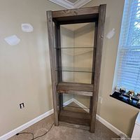 Wood etagere shelf bookcase with glass shelves and built-in light, shown upright in corner of room.