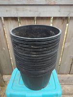 Stack of 15 black plastic planting pots shown from side, stacked one inside another, showing their cylindrical shape and size.