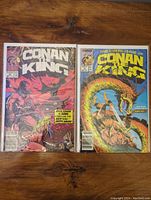 Two Conan the King comics, issues #54 and #55, placed side by side on a wooden surface.
