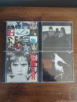 Four U2 CD album cases: Achtung Baby, The Joshua Tree, War, and Rattle and Hum, displayed on wooden surface.