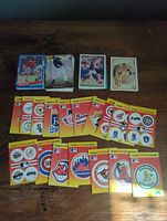 Photo showing multiple stacks of baseball cards and team logo sticker cards laid out on a wooden surface.