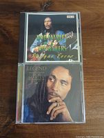 Front of two CDs 'Reggae Fever Vol. 3' and 'Legend' by Bob Marley and the Wailers on wooden surface.